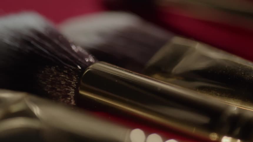 Makeup brushes with dark bristles and gold handles on a red surface