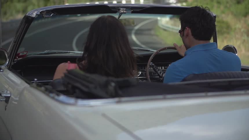 Man and women driving in a convertible down a road