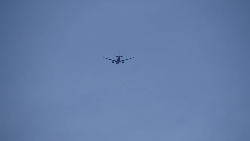 An airplane with blinking lights flies away through the clouds at dusk