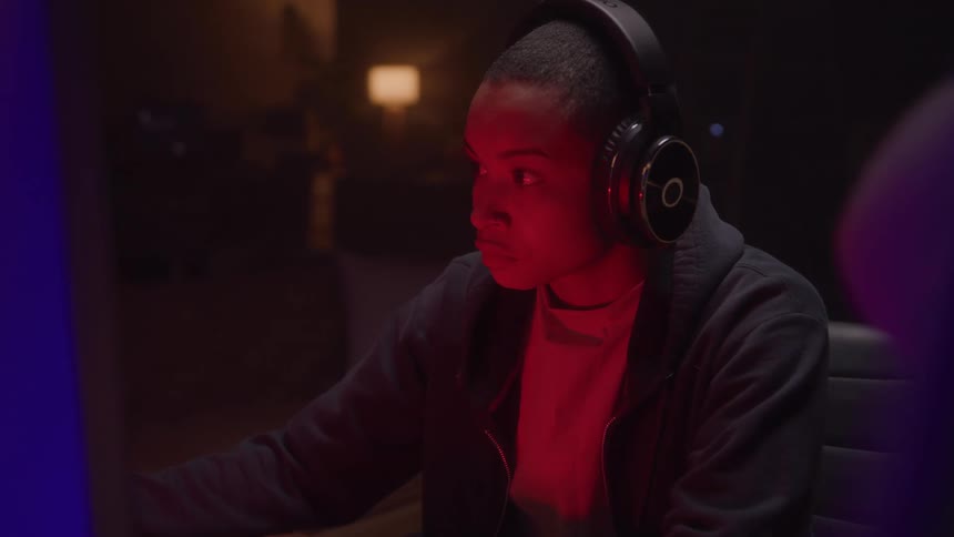 Person wearing headphones focused in front of a screen illuminated by red light