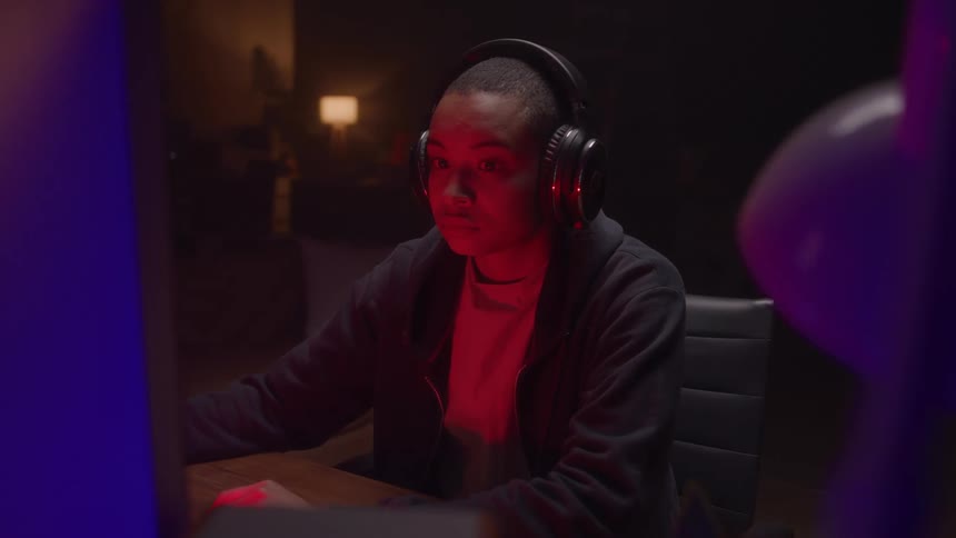 Woman with headphones concentrating in front of computer under red and blue light
