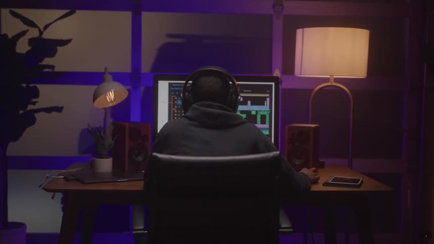 A young man wearing a headset sits at a computer illuminated by lamps on both his left and right sides