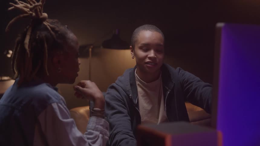 Two women collaborate in front of a monitor in a softly lit environment