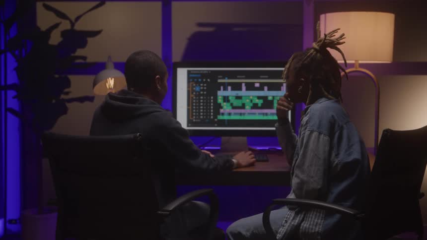 Two young black women discussing while working together with a desktop computer in a music studio