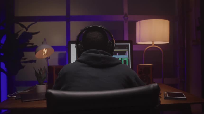 Person works on a computer with headphones in a dim warmly lit room