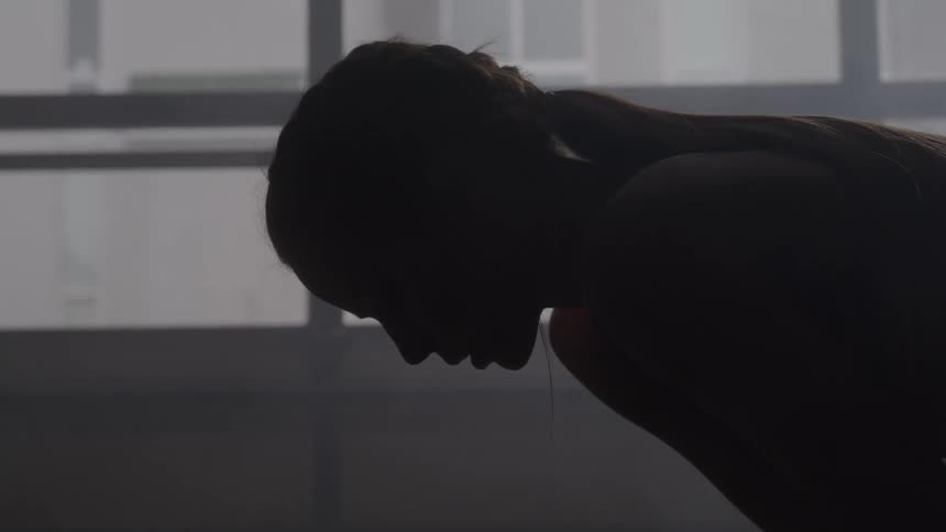 Close up of a young woman bending to rest after a fitness session in a room during daytime