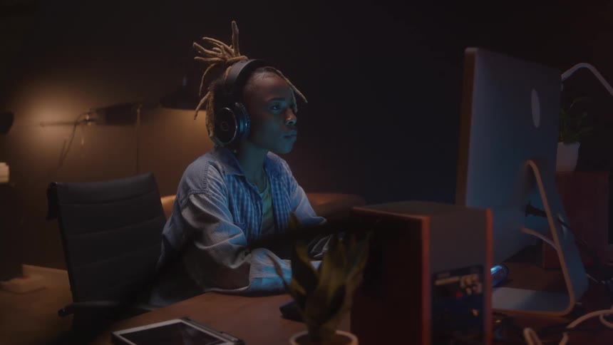 Person wearing headphones smiles while working on a computer in a dimly lit room