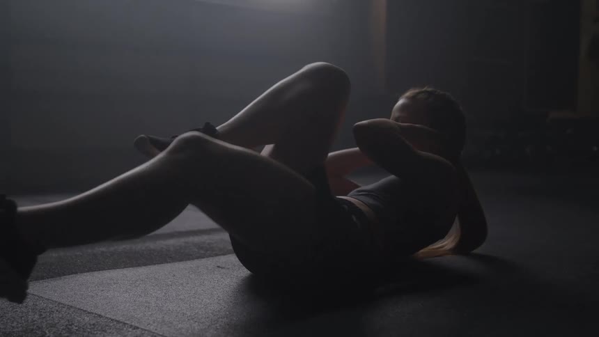 Woman performing bicycle crunch in a dimly lit room with soft light coming through the window