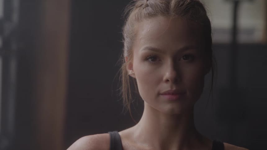 A woman gazes at the camera in a softly lit gym