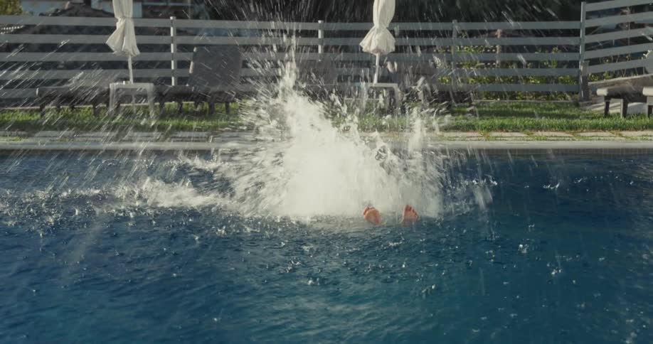 Boy jumping into swimming pool in backyard at night