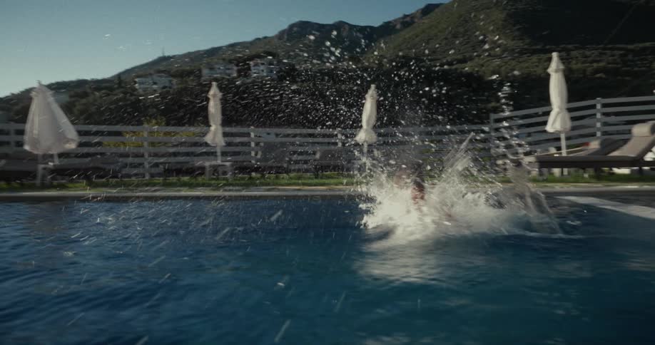 A young child wearing swimming goggles runs and jumps into a swimming pool at midday