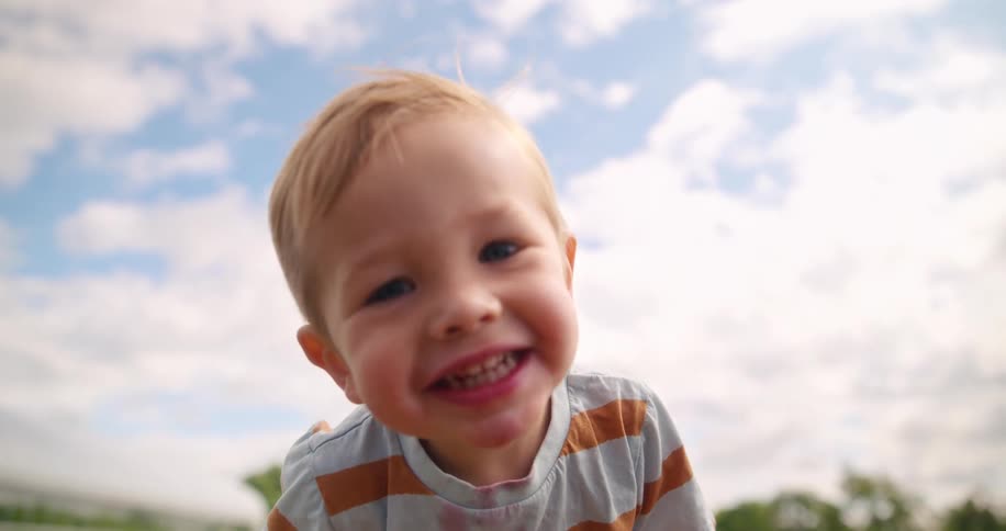 Blond child smiles with a dirty face and striped shirt outdoors under a blue sky with clouds