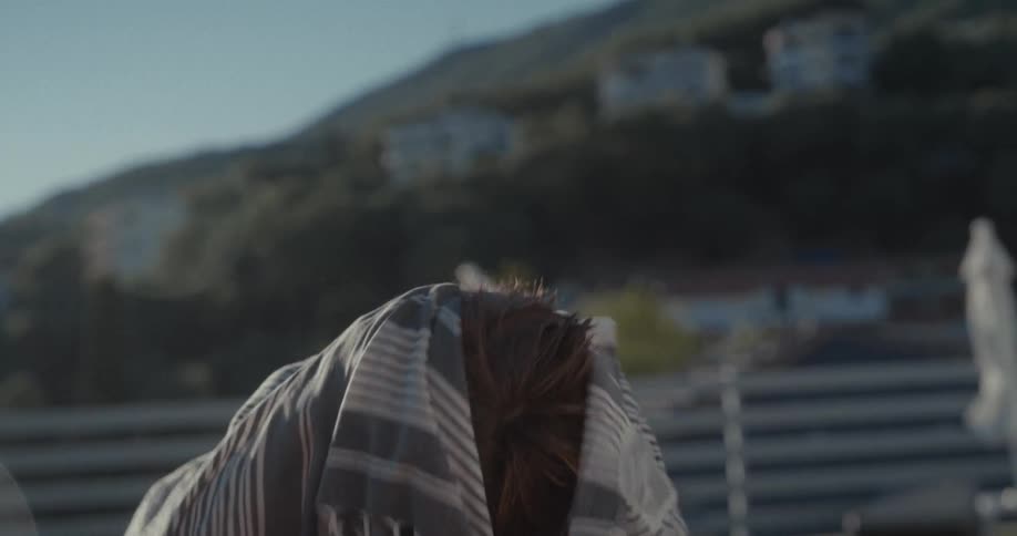 A boy child drying his face and hair with clothing after stepping out of an outdoor pool during daytime