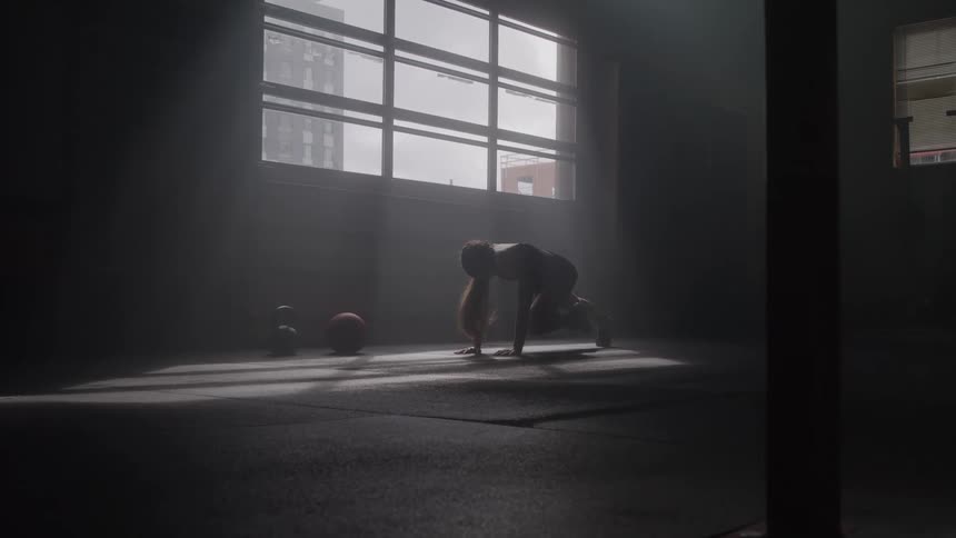 Woman works out alone in a dim gym lit by natural light streaming through the window
