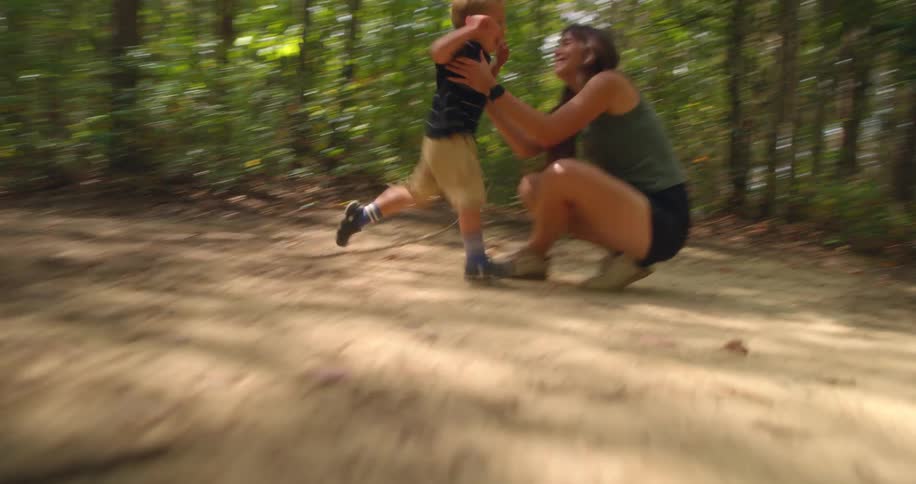 A young boy playfully runs into his mothers arms while hiking in the woods