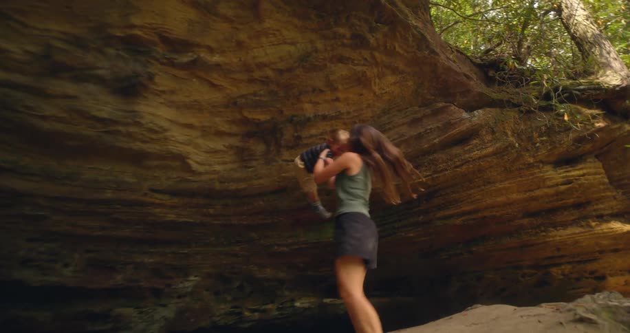 Woman spinning a child in her arms outdoors near rocky formations