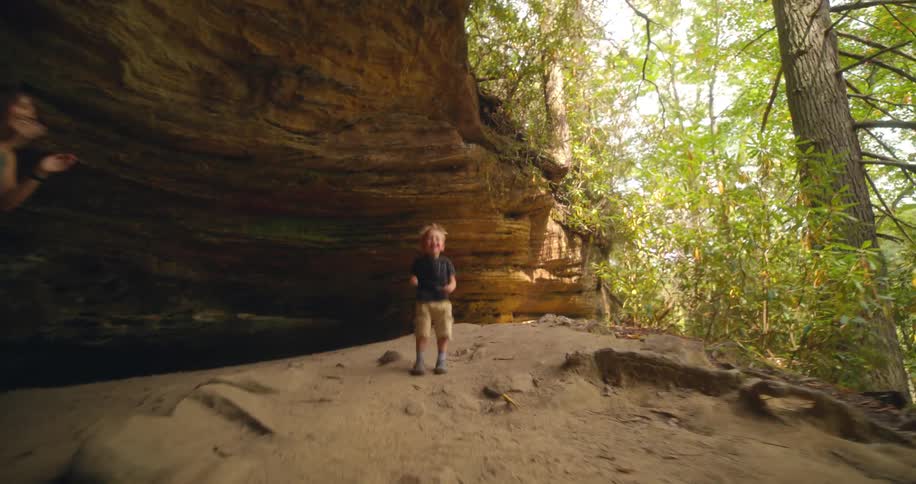 Mother and son jumping and playing together at a cave entrance in a woodland during daytime