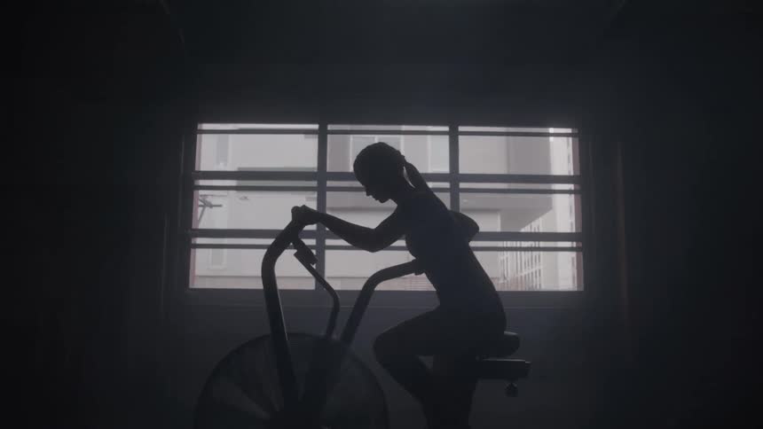 Woman exercises on a stationary bike in a dark and quiet setting