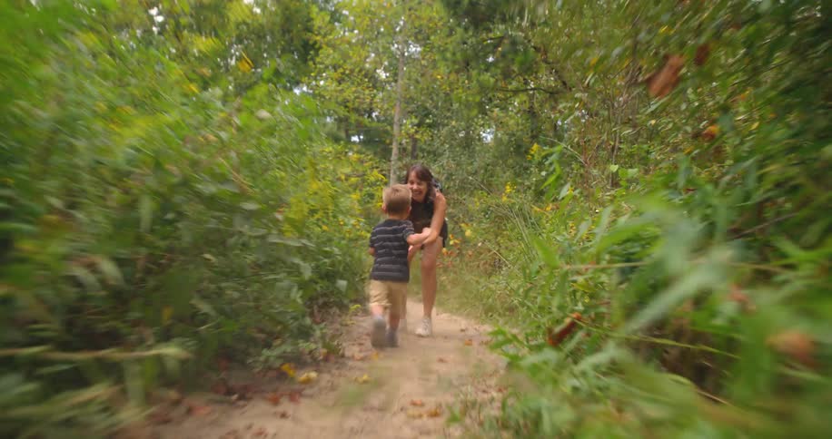 A male toddler playfully runs into his sisters arms as she stands on a trail in a woodland area during daytime