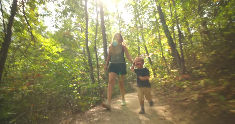 A young woman and a child run hand in hand along a forest trail at midday their faces lit with excitement