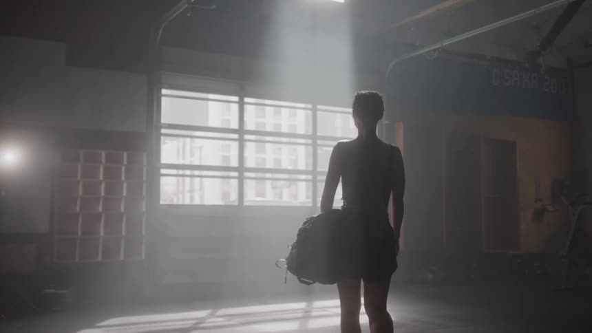 A young woman walks into the gym at midday carrying a bag as she heads toward the window