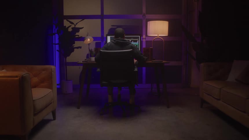 A young black male sits behind a computer then stands up removes his headset and walks away from the desk