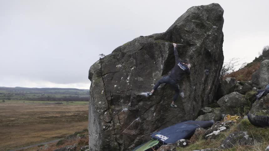 Climber tackles a large boulder amid an open landscape on a cloudy day