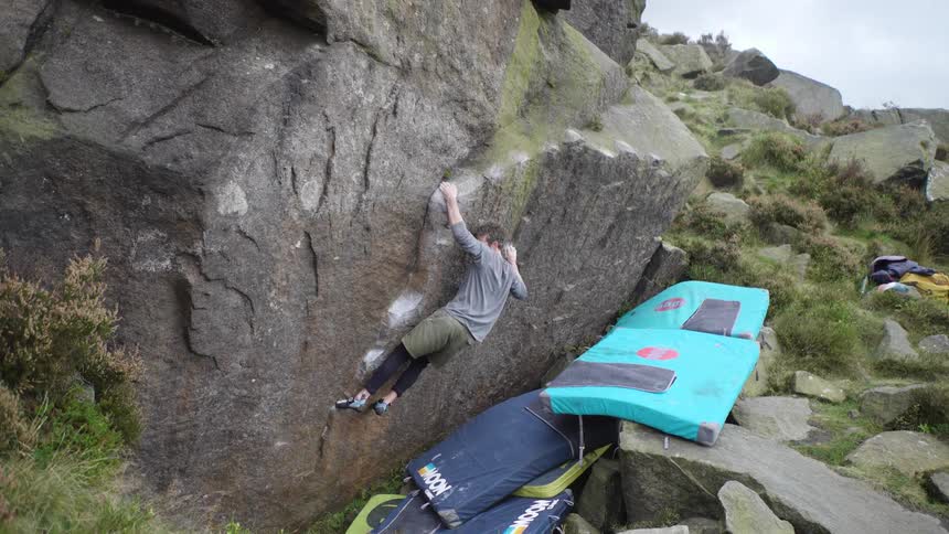 A man boulders on a large outdoor rock face with crash pads below