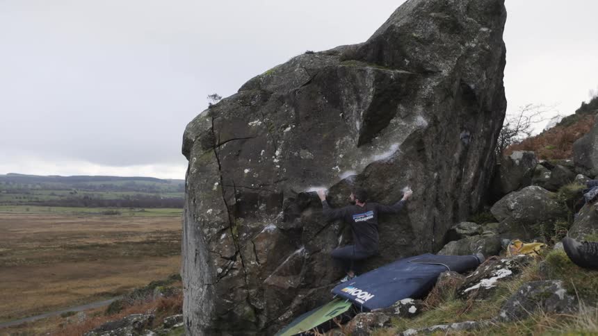 Man begins climbing a large boulder with crash pads on the ground