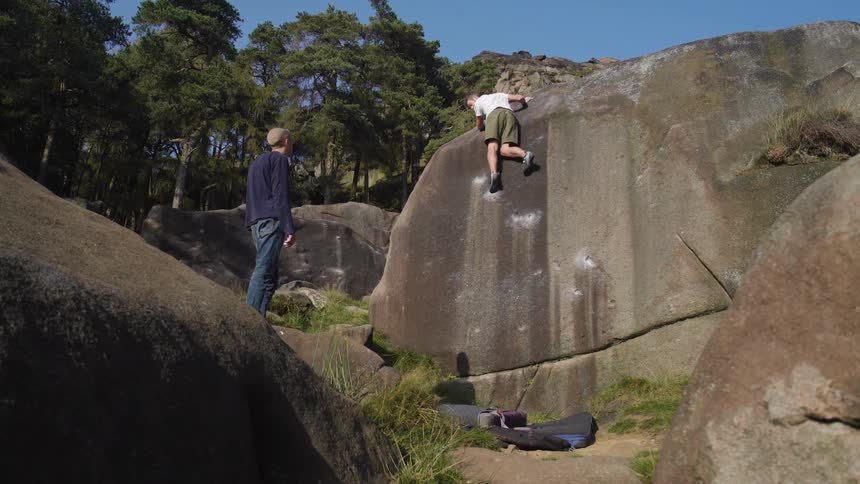 A man boulders up a large rock as another watches nearby