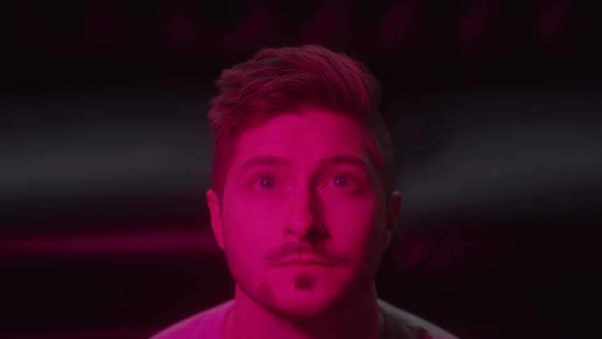 A closeup portrait of a young man with styled hair and a short beard transitions through a sequence of vibrant blue green and red light colors against a dark background