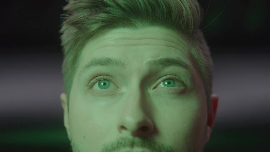 A young man bathed in changing colored light gazes upward with curious slightly awed eyes