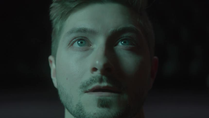 A young man bathed in different changing colored lights gazes upward eyes wide with quiet wonder