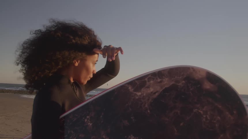 Woman with surfboard gets ready on the beach at sunset