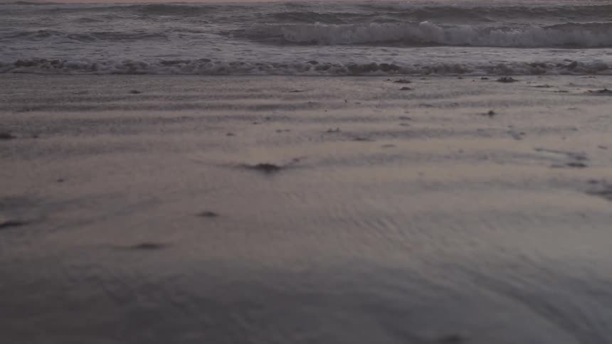 Waves flow onto the beach under a red tinted sky