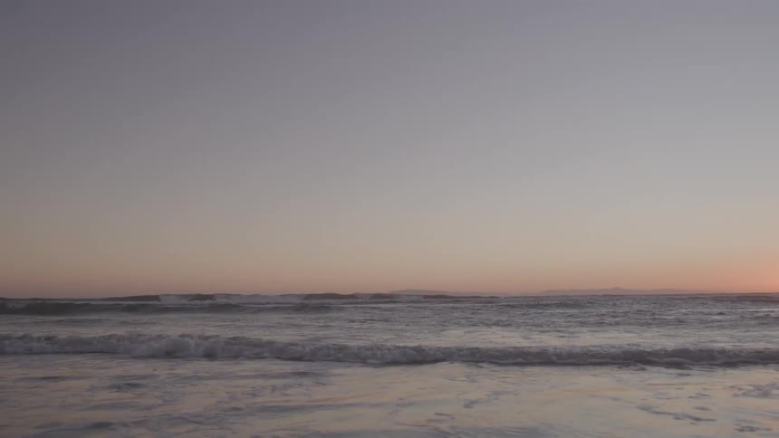 Gentle waves approach the shore during sunset