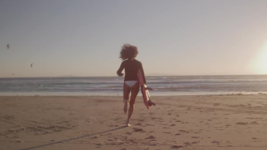 Woman runs across the sand towards the sea with a surfboard