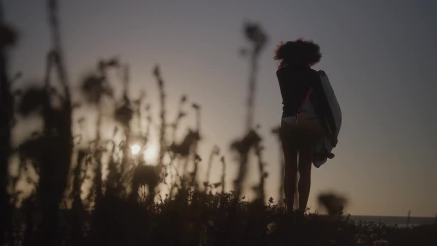Woman stands among wildflowers on the coast while holding a boogie board