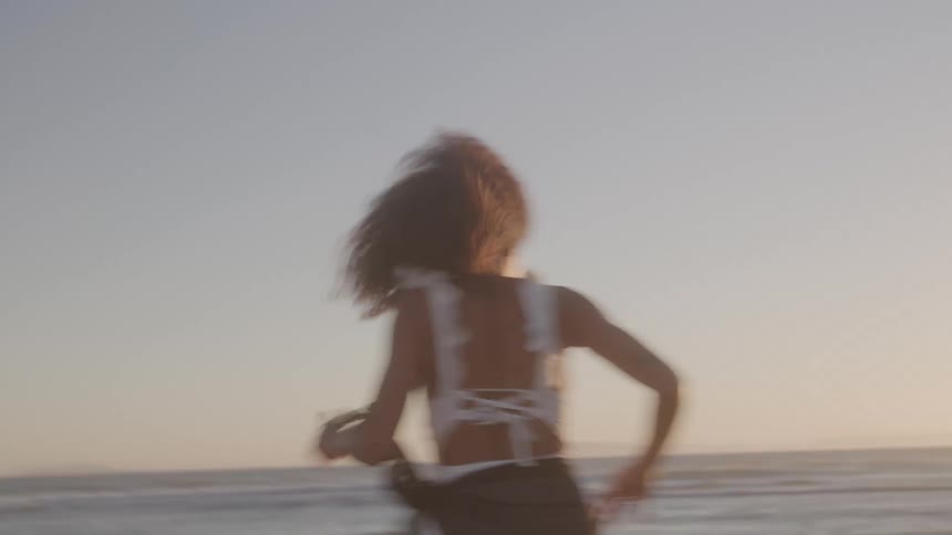 Woman runs barefoot toward the sea at sunset
