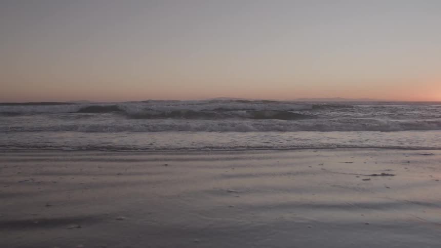 Gentle waves reach the shore at sunset on the horizon