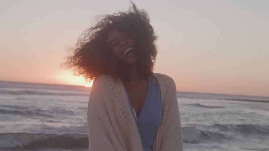 Woman smiles by the sea with the sunset in the background