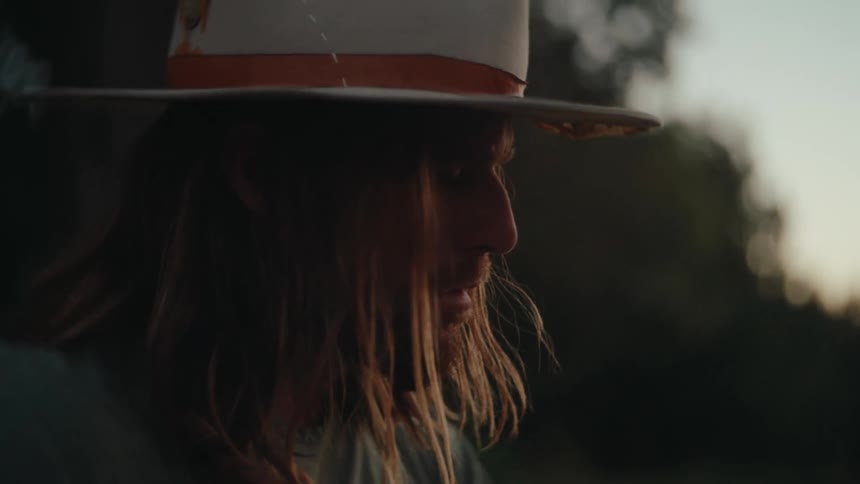 Man in a hat looks thoughtfully downward under the soft evening light