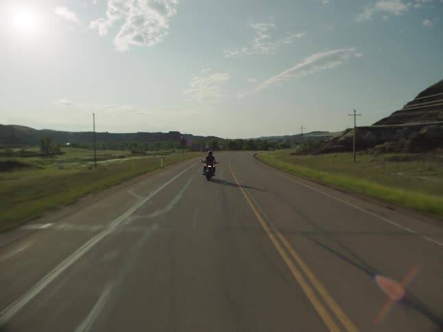 Motorcyclist rides along a road surrounded by green fields on a sunny day