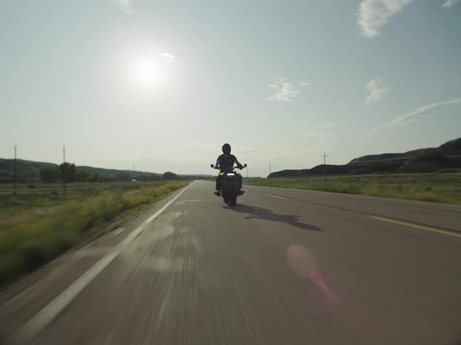 Motorcyclist rides along an open road lit by the afternoon sun