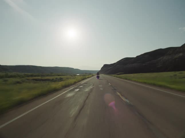 A person rides a motorcycle on a countryside highway at midday wearing a helmet
