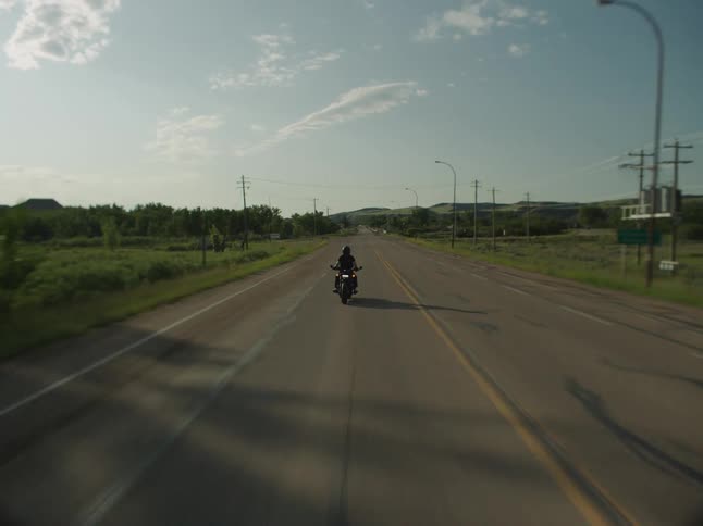 Motorcyclist rides along a road surrounded by vegetation on a sunny day