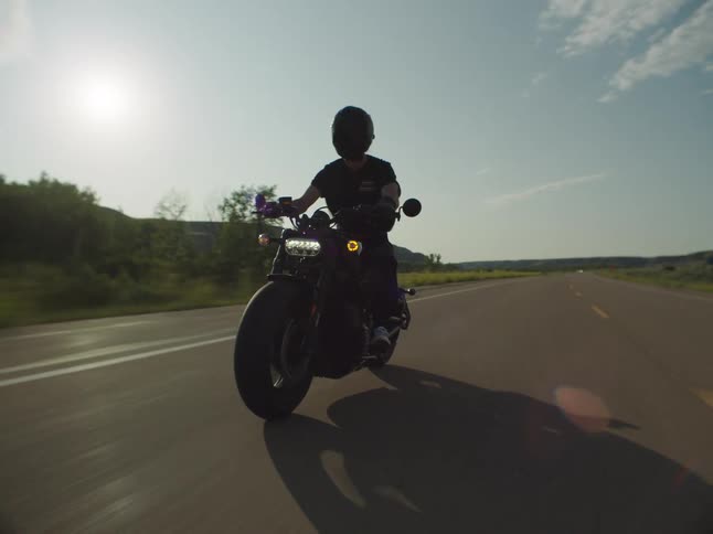 Motorcyclist speeds along an open road under the strong afternoon sun