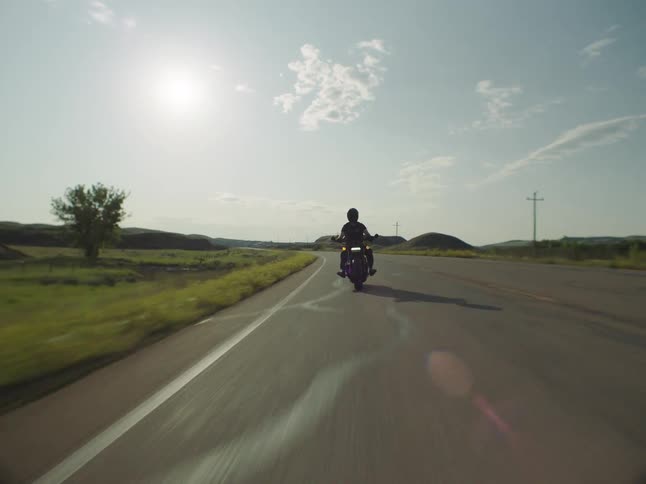A person rides a motorcycle at top speed on the freeway at midday wearing a helmet