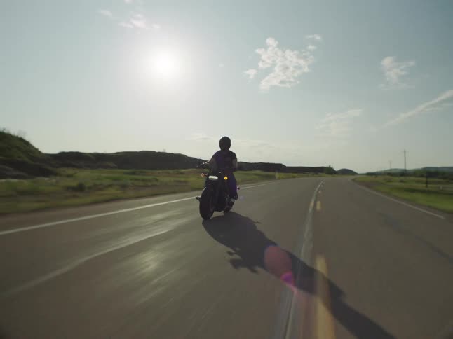 Motorcyclist rides along an open road under the sun on a clear day