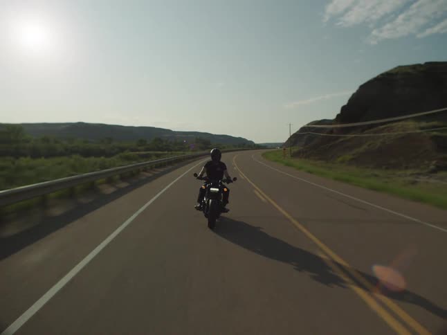An adult rides a motorcycle on a rural highway on a summer day